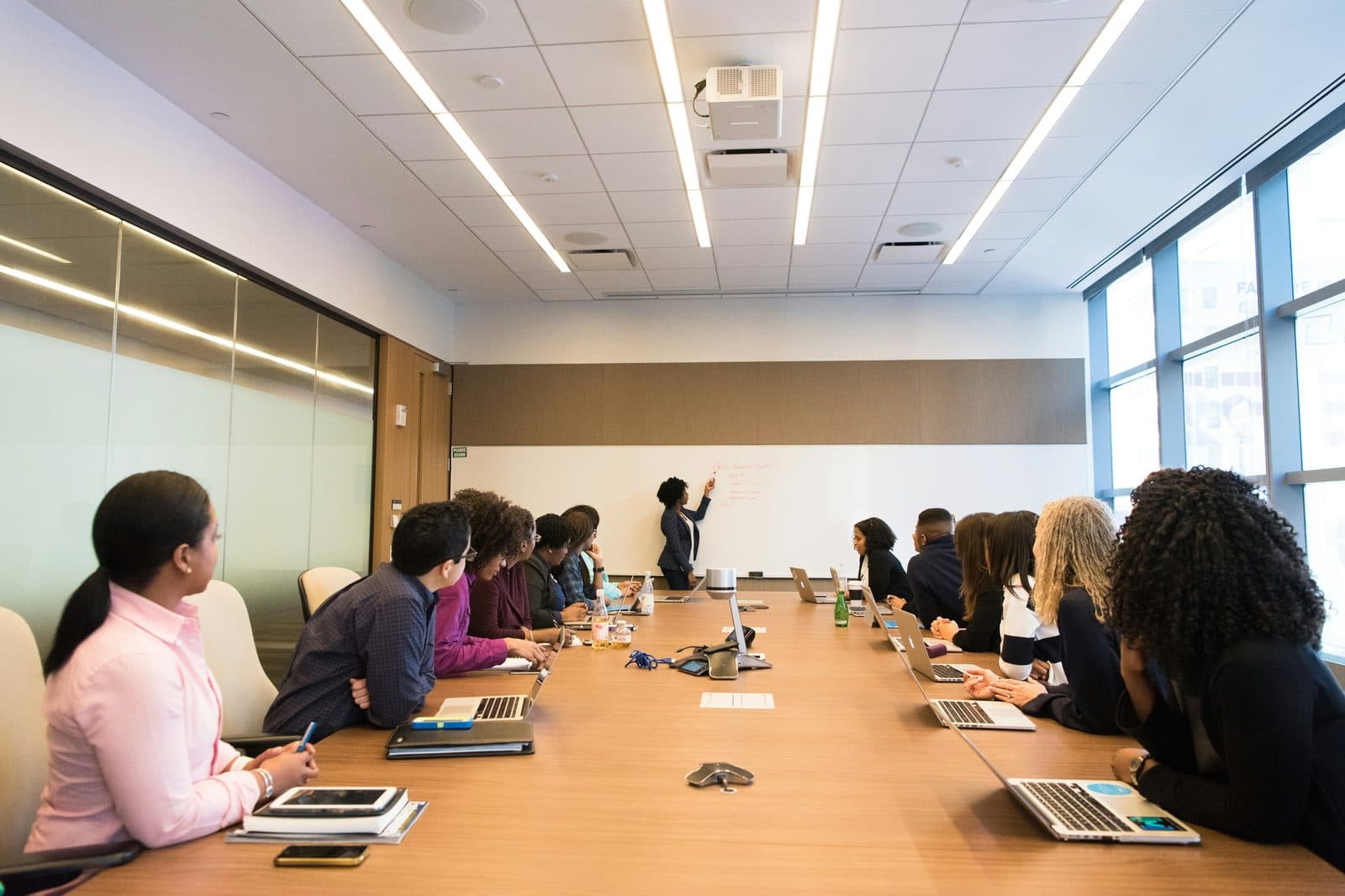 A diverse professional team meeting around a conference table with an active whiteboard.