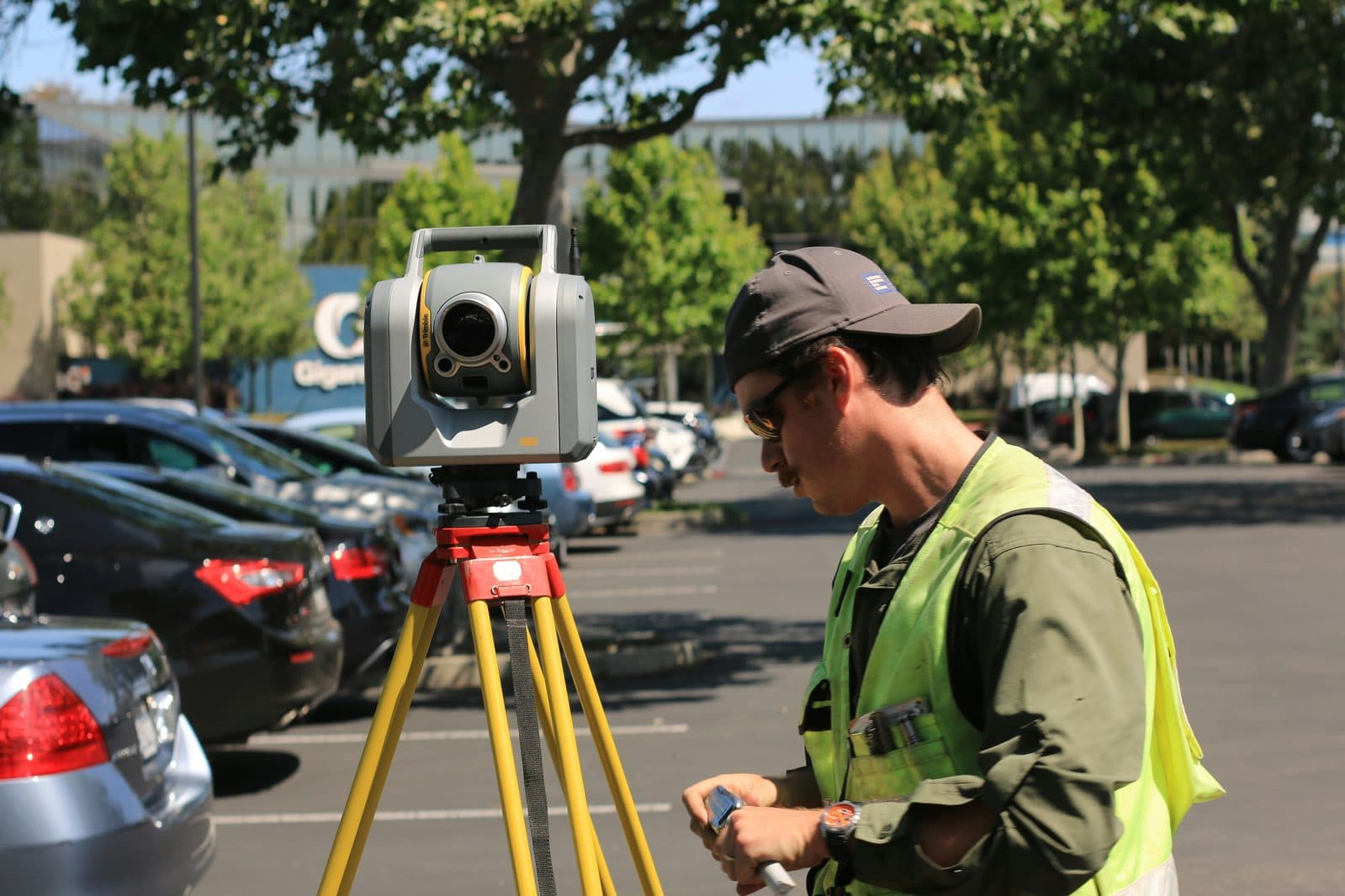A field surveyor operating a total station in a commercial parking lot.